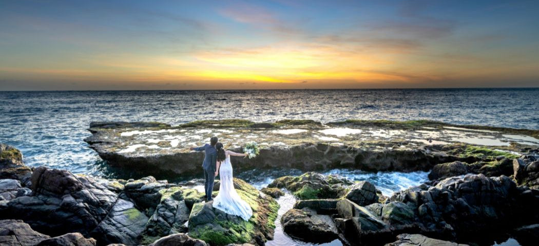 Couple standing on rocky beach at sunset