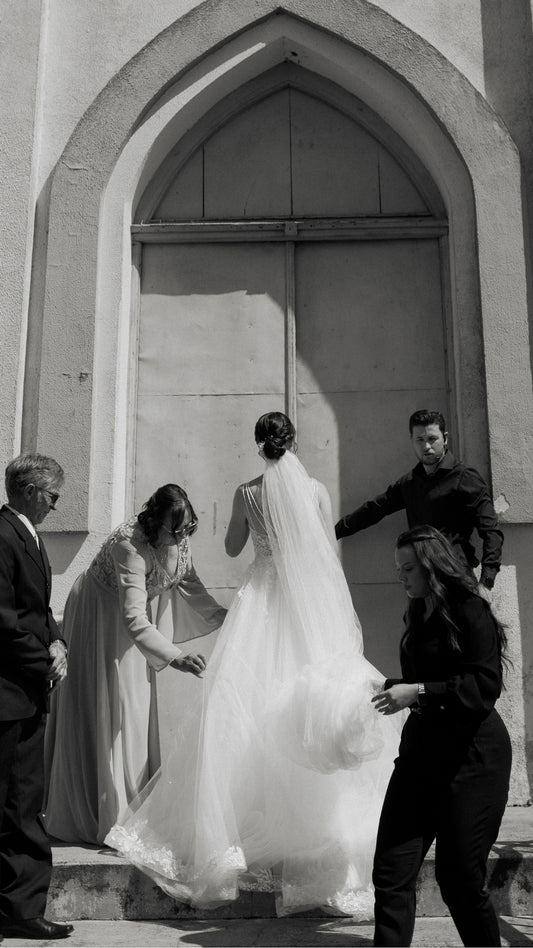Attendants helping a bride through a stone doorway.