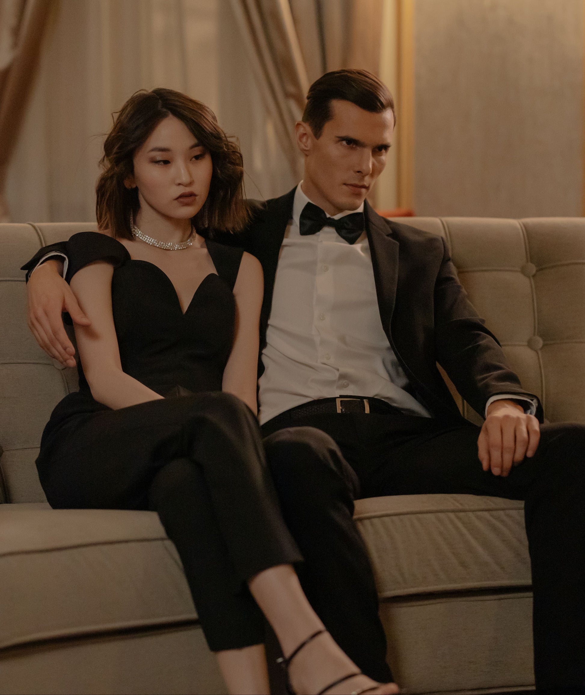 Man and woman in formal attire sitting on a couch in an elegant room.